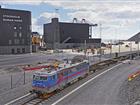 Tåg på spår med byggnader och kranar i bakgrunden