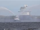Bogserbåten Montfred vattensaluterar Main Schiff 1 på väg in i hamn